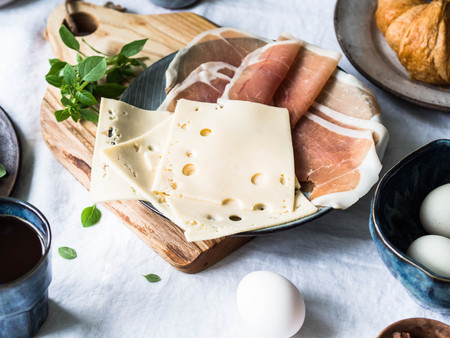 Different ingredients for breakfast. Cheese, prosciutto, eggs, avocado, coffee milk basil croissants Top viewの写真素材