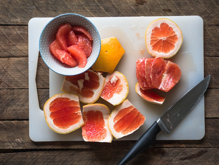 Peeled and sliced grapefruit on a white board on a woodenの写真素材