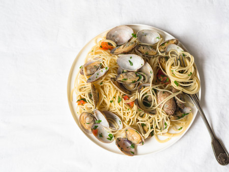 Spaghetti with clams, tomatoes, garlic and parsley on a white plate and rustic fork on a whiteの写真素材