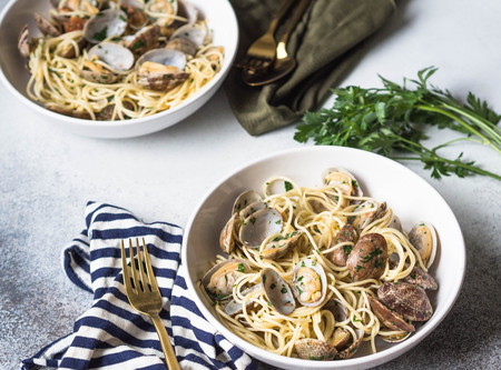Spaghetti with clams, garlic and parsley in a white bowls, napkins and gold appliancesの写真素材