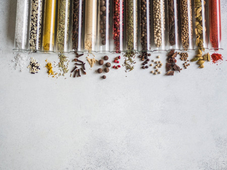 Various dry spices in glass tubes and spilled on gray background.の写真素材
