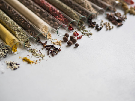 Various dry spices in glass tubes and spilled on gray background.の写真素材