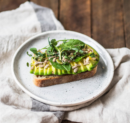 Green healthy sandwich made from spinach, sprouts, avocado and various seeds on a white plateの写真素材