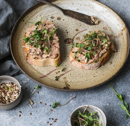 Two toasts duck with prunes rillettes pate on white bread with sprouts and various seeds on a vintage plateの写真素材
