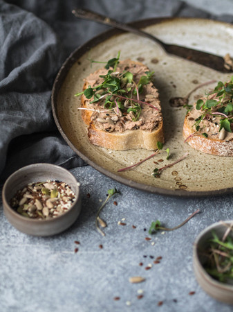 Two toasts duck with prunes rillettes pate on white bread with sprouts and various seeds on a...