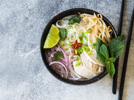 Traditional Vietnamese soup- pho ga in black bowl with chicken and rice noodles, mint and cilantro,...