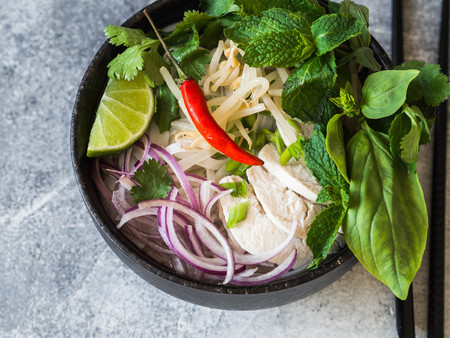 Traditional Vietnamese soup- pho ga in black bowl with chicken and rice noodles, mint and cilantro,...
