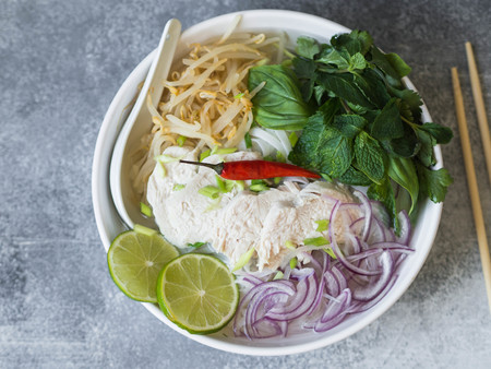 Traditional Vietnamese soup- pho ga in white bowl with chicken and rice noodles, mint and cilantro,...