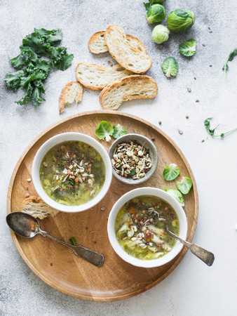 Green vegetable vegan soup from keil, brussels sprouts, zucchini, leek with various germinated seeds and sprouts with croutons on wood tray on lightの写真素材