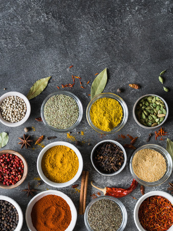 Various dry spices flat lay in small bowls on gray