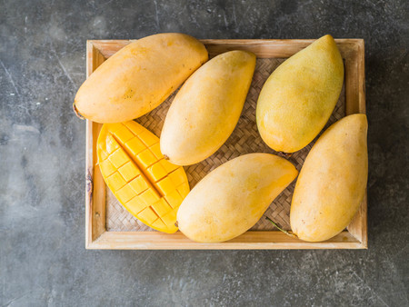 Several Fresh sweet yellow Thai mangoes on a wooden tray on a grayの写真素材