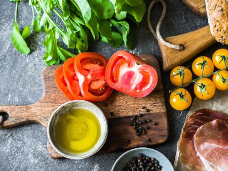 Various fresh ingredients for making sandwiches - vegetables - tomatoes and arugula, bread, prosciutto, olive oil on dark background.の写真素材