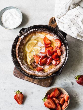 Dutch baby pancake dusted with powdered sugar with fresh strawberries in a black frying pan. Top viewの写真素材