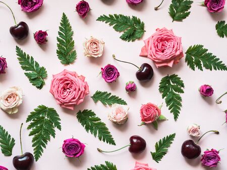 Flat lay composition of green fern leaves, cherries and roses of varying size and color on pinkの写真素材