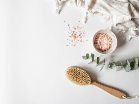 Body brush with wooden handle, white towel and a bowl with pink sea salt on white background. copy space.の写真素材