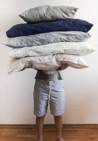 Uncertain man holds large pillows of various colors against a white wallの写真素材