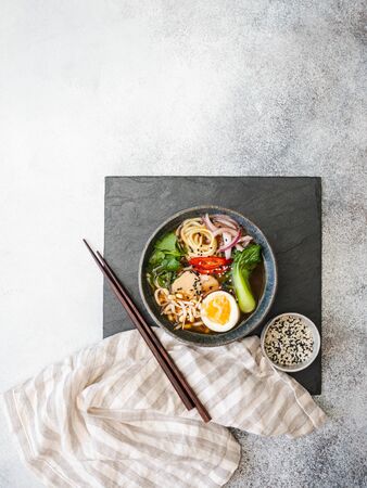 Asian Ramen noodles with chicken, pak choi cabbage and egg on black slate board on grey background. Top view. Copy spaceの写真素材