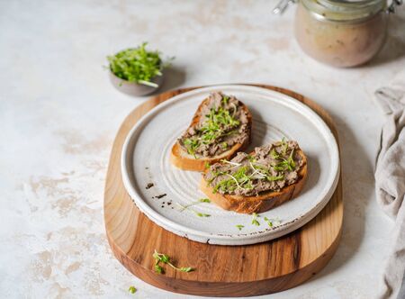 Two toasts chicken rillettes (pate) on white bread with sprouts on white plate on wood cutting board