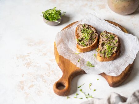 Two toasts chicken rillettes (pate) on white bread with sprouts on white plate on a wood cutting boardの写真素材
