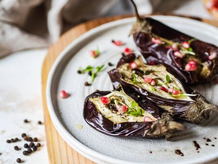 Baked eggplants slices with spices, sprouts, pomegranate and olive oil on a white ceramic plate on a grayの写真素材
