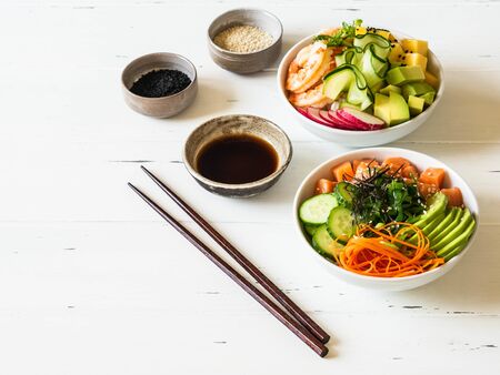 Two different Hawaiian poke bowl with seafood and fresh vegetables and fruits and rice on a white wooden backgroundの写真素材