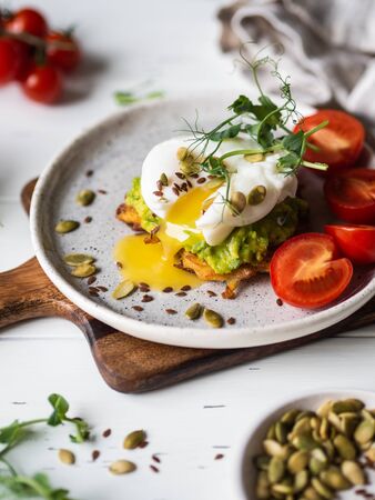 Healthy nutritious breakfast of potato pancake, mashed avocado, poached egg, pea sprouts and various seeds on ceramic plateの写真素材
