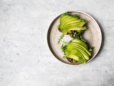 Healthy homemade toasts with arugula and avocado on rye grain bread on plate on grey background. Top...