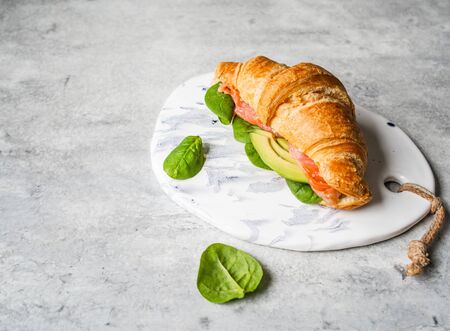 French croissant with salmon slices, avocado and spinach on white ceramic board on grey background.の写真素材
