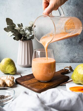 Hand with glass jug pours into a glass of fresh healthy carrot, pear, ginger smoothie with chia seedsの写真素材