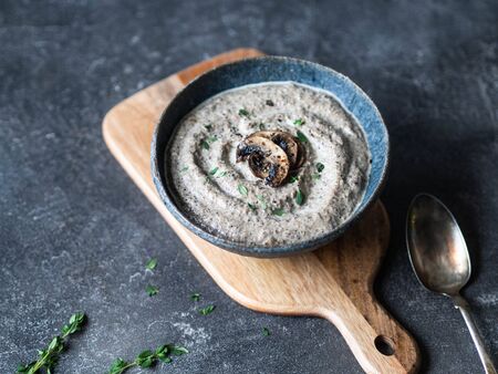 Champignon mushroom cream soup with fresh thyme in blue bowl on wood cutting board. Copy space