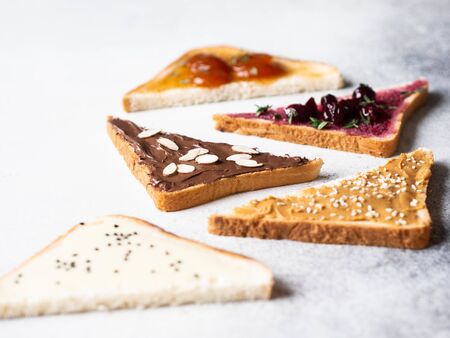 Various sweet toasts with chocolate paste, condensed milk, peanut butter and fruit apricot jam, sprinkled with sesame seeds, almond flakes and fresh thymeの写真素材