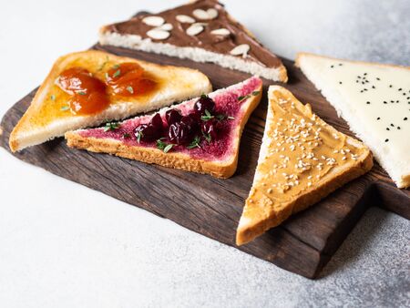 Various sweet toasts with chocolate paste, condensed milk, peanut butter and fruit apricot jam, sprinkled with sesame seeds, almond flakes and fresh thymeの写真素材