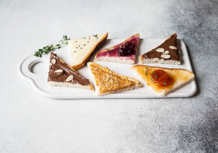 Various sweet toasts with chocolate paste, condensed milk, peanut butter and fruit apricot jam, sprinkled with sesame seeds, almond flakes and fresh thyme.の写真素材