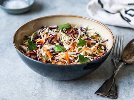 Red cabbage, carrot, cabbage coleslaw salad in blue bowl on grey background.の写真素材