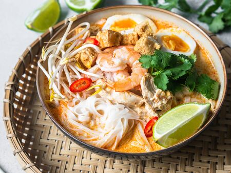 Malaysian noodles laksa soup with chicken, prawn and tofu and herbs in a bowl on grey backgroundの写真素材
