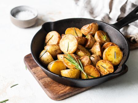 Black cast iron pan with fried roasted potato wedges with herbs on light backgroundの写真素材