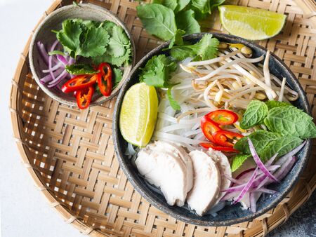 Traditional Vietnamese soup- pho ga in bowl with chicken and rice noodles, mint and cilantro, red...