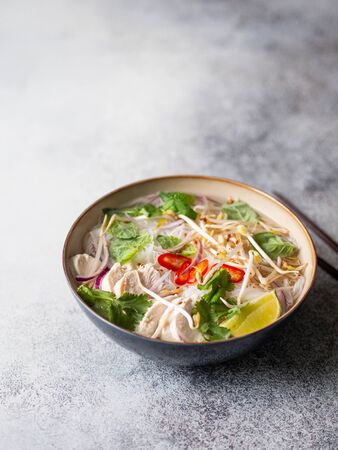 Traditional Vietnamese soup- pho ga in bowl with chicken and rice noodles, mint and cilantro, red...
