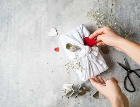 Eco-friendly fabric reusable gift packaging with Eucalyptus, white flowers and red wood heart. Valentine's day reusable sustainable gift wrapping alternative. Zero waste concept.の写真素材