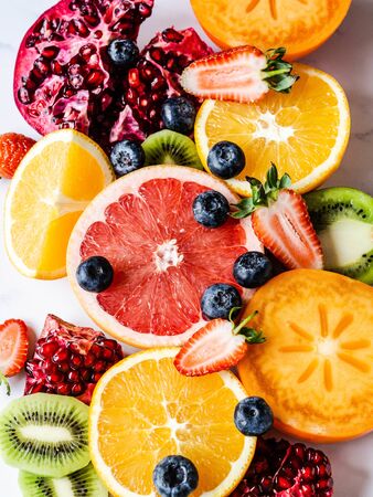 Multicolored seasonal healthy natural fruit composition with persimmon, blueberries, orange, kiwi, strawberries, grapefruit, pomegranate, orange slices. Top viewの写真素材