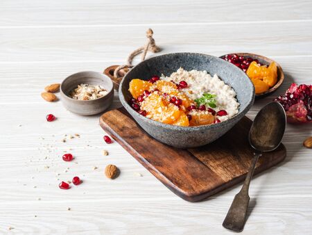 Oatmeal with fresh tangerine slices and pomegranate seeds, ground almonds and mint in a blue bowl on white background. Copy space.の写真素材
