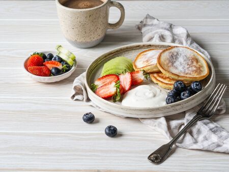 Delicious breakfast - fritters pancakes, sprinkled with powdered sugar with fruits and berries and sour cream on plate on wood table. Copy spaceの写真素材