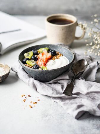 Delicious breakfast - the cup of coffee and granola with yogurt and berries and open magazine on the table. Copy space.の写真素材
