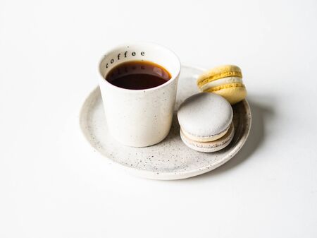 Two pastel macaroons with white ceramic cup of black coffee on ceramic plate on white background. Copy spaceの写真素材