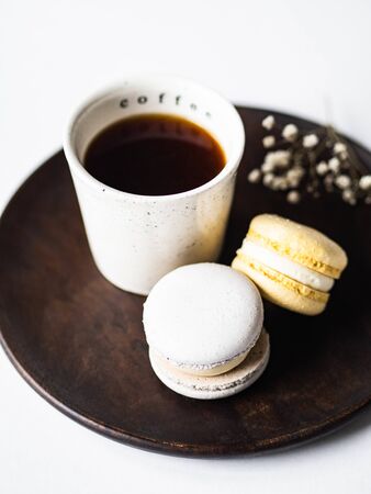 Two pastel macaroons with white ceramic cup of black coffee on wood plate on a white backgroundの写真素材
