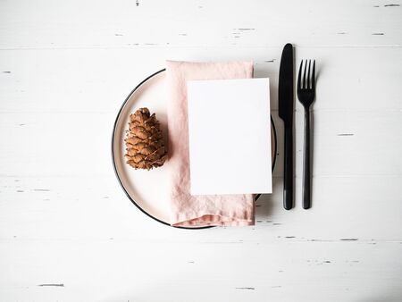 Rustic table with Christmas setting with plate, pink napkin, menu card and appliances on white wood table.の写真素材