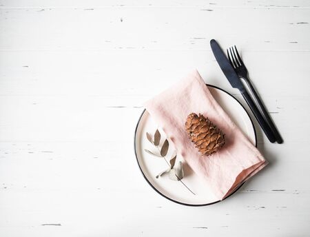 Rustic table setting with plate, pink napkin, cone, eucalyptus and appliances on white wood table.の写真素材