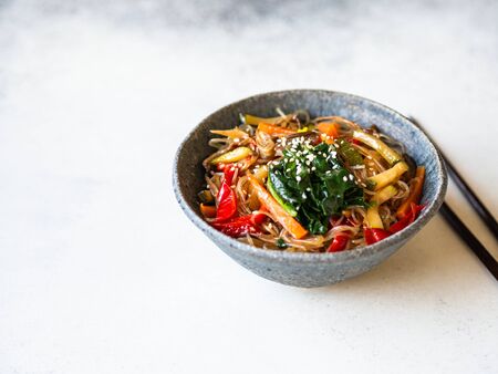 Blue bowl with rice noodles and various vegetables steer fry on a grey background. copy space