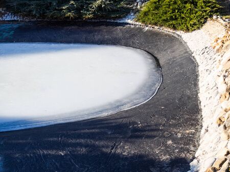 Large pond in garden with frozen water. Home-made pond and ice inside it in winterの写真素材