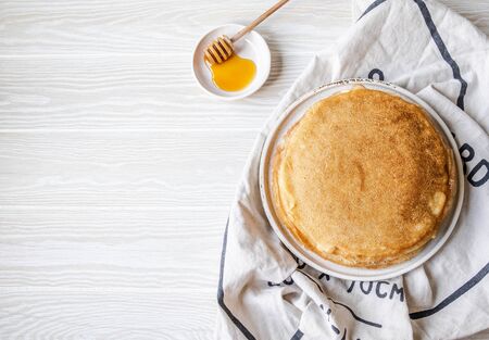 Stack Russian homemade thin pancakes on white plate and wood honey spoon and honey on small white plate. Traditional wheat pancakes for Shrovetide. Top view.の写真素材